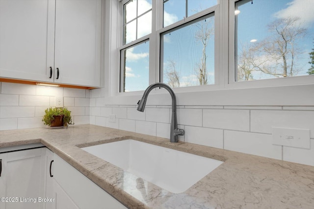 room details with tasteful backsplash, light stone countertops, white cabinetry, and a sink