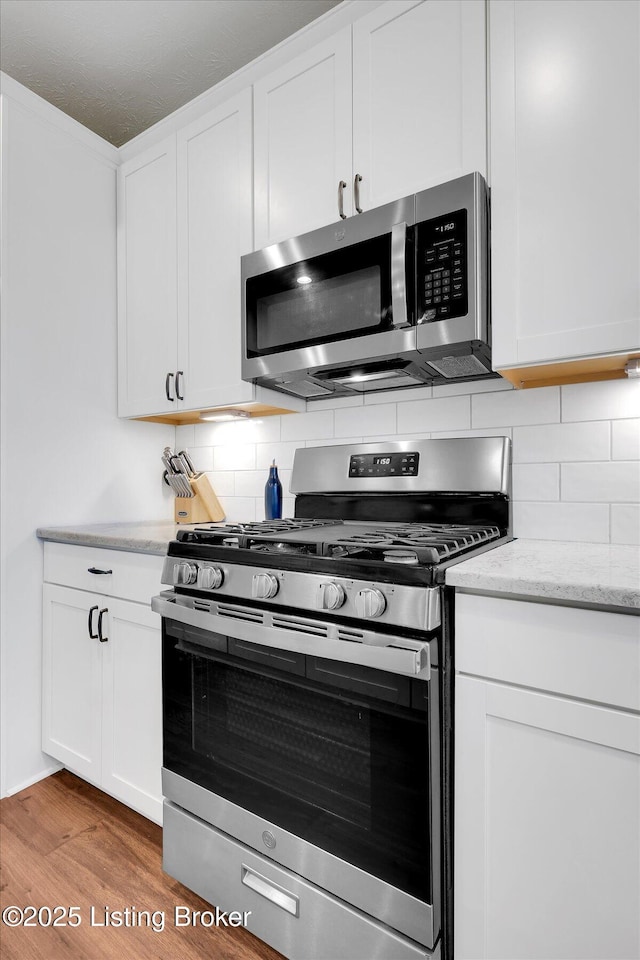 kitchen with white cabinets, light stone countertops, decorative backsplash, stainless steel appliances, and light wood finished floors
