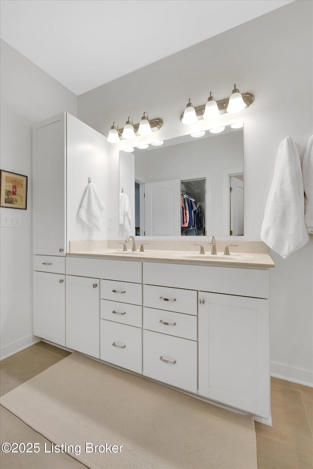 bathroom with baseboards, a walk in closet, a sink, and double vanity