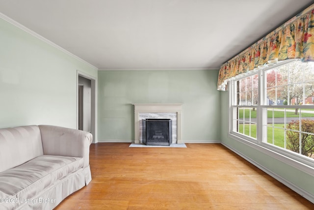 living room featuring baseboards, light wood-type flooring, crown molding, and a premium fireplace