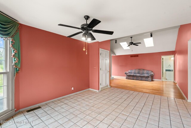 interior space featuring visible vents, ceiling fan, vaulted ceiling with skylight, and light tile patterned flooring