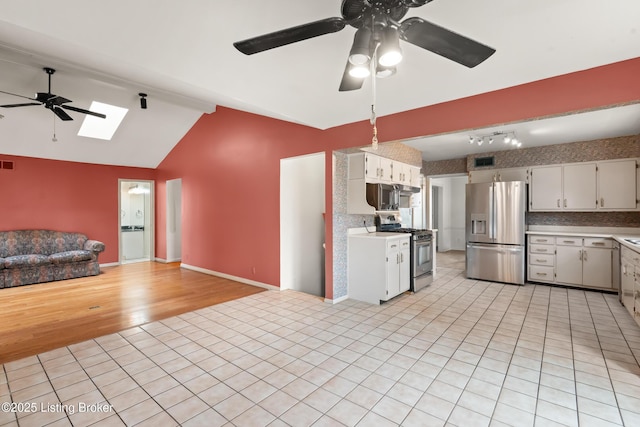 kitchen with vaulted ceiling with skylight, open floor plan, light countertops, a ceiling fan, and stainless steel appliances