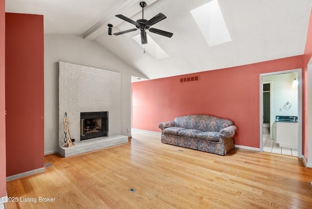 living room with visible vents, vaulted ceiling with skylight, ceiling fan, a fireplace, and wood finished floors