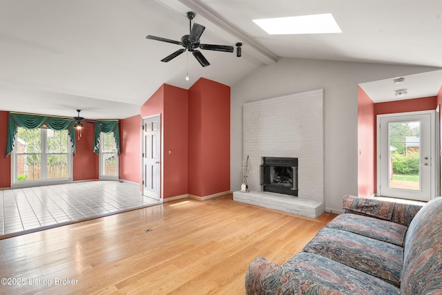 living area featuring baseboards, a brick fireplace, ceiling fan, lofted ceiling with skylight, and wood finished floors