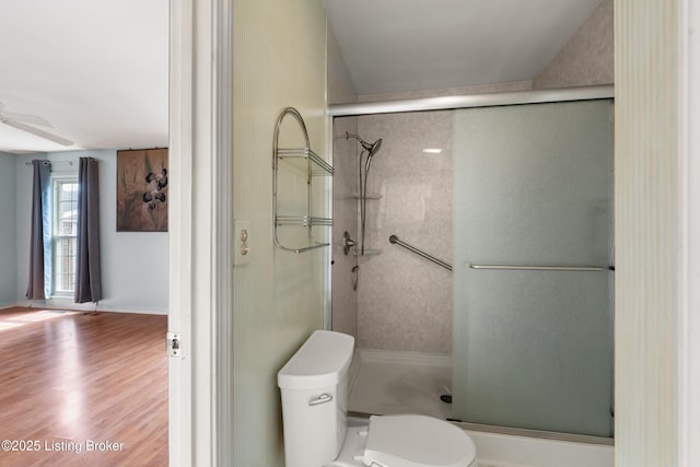 bathroom with toilet, ceiling fan, a stall shower, and wood finished floors