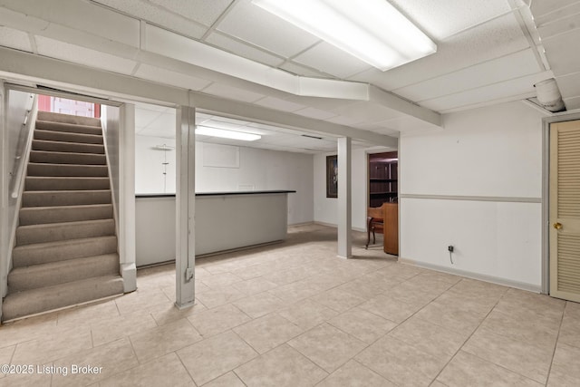 below grade area with a paneled ceiling, light tile patterned flooring, and stairs