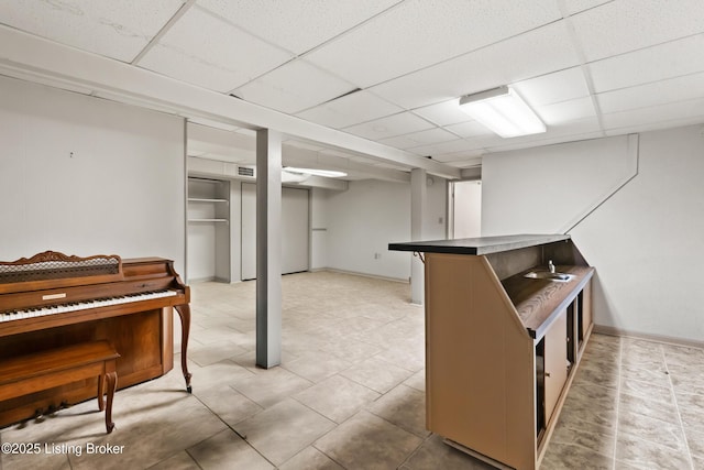 finished below grade area featuring a sink, light tile patterned floors, baseboards, and a paneled ceiling