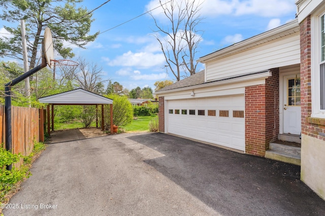 garage featuring a carport, driveway, and fence