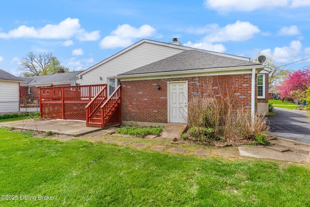 rear view of property with roof with shingles, brick siding, a deck, and a yard