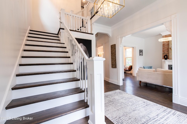 stairway with baseboards, arched walkways, an inviting chandelier, crown molding, and wood finished floors