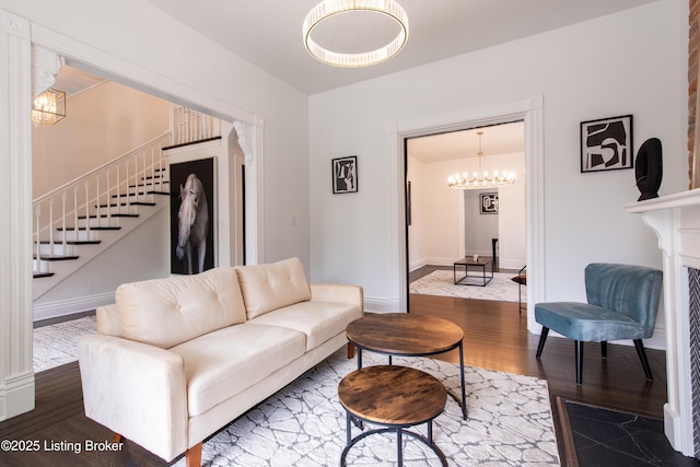 living area featuring a chandelier, wood finished floors, baseboards, and stairway