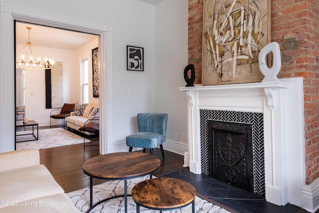 living area featuring a fireplace with flush hearth, wood finished floors, brick wall, and a notable chandelier