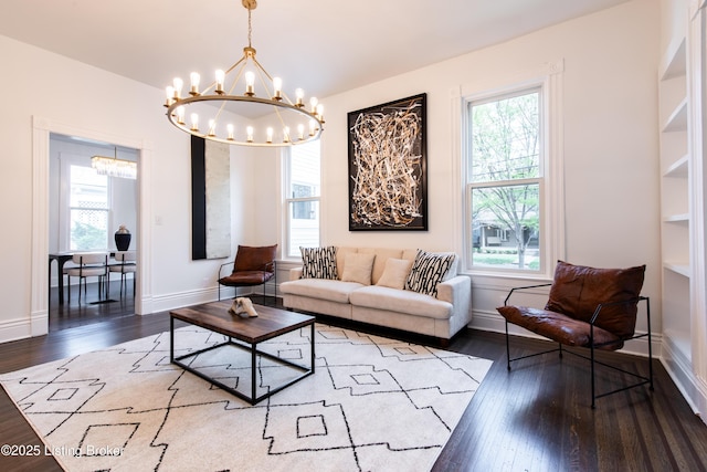 living area featuring a wealth of natural light, an inviting chandelier, hardwood / wood-style flooring, and baseboards