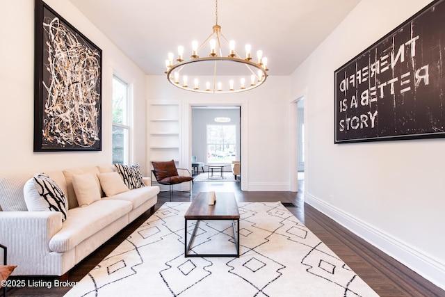 living area with baseboards, a notable chandelier, wood finished floors, and a healthy amount of sunlight