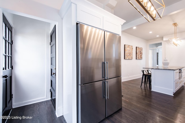 kitchen with dark stone countertops, white cabinets, dark wood-style floors, high end fridge, and a breakfast bar area