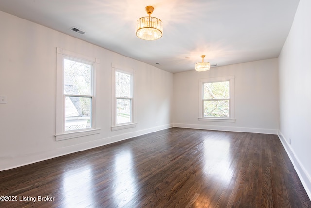 empty room featuring dark wood-type flooring, an inviting chandelier, baseboards, and visible vents