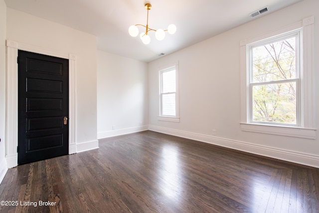 spare room featuring baseboards, a notable chandelier, dark wood finished floors, and visible vents