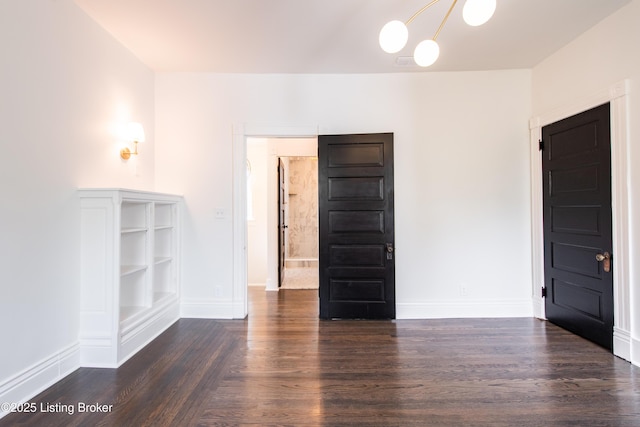 empty room with baseboards, an inviting chandelier, and dark wood finished floors