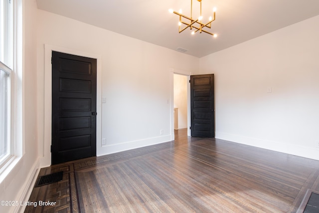spare room featuring visible vents, baseboards, an inviting chandelier, and dark wood-style floors
