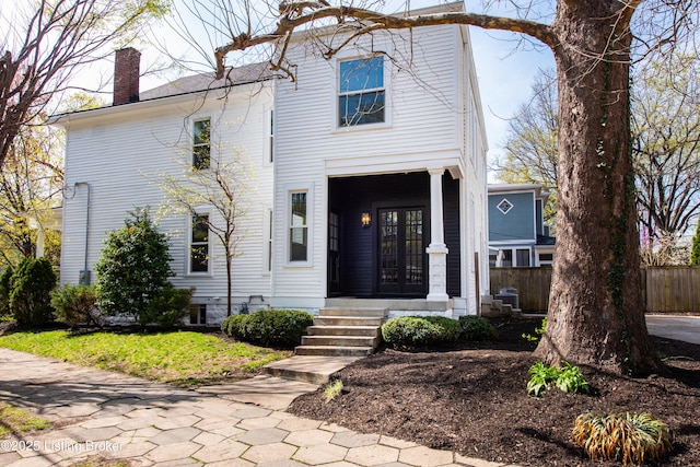 view of front of property with a porch, french doors, fence, and a chimney