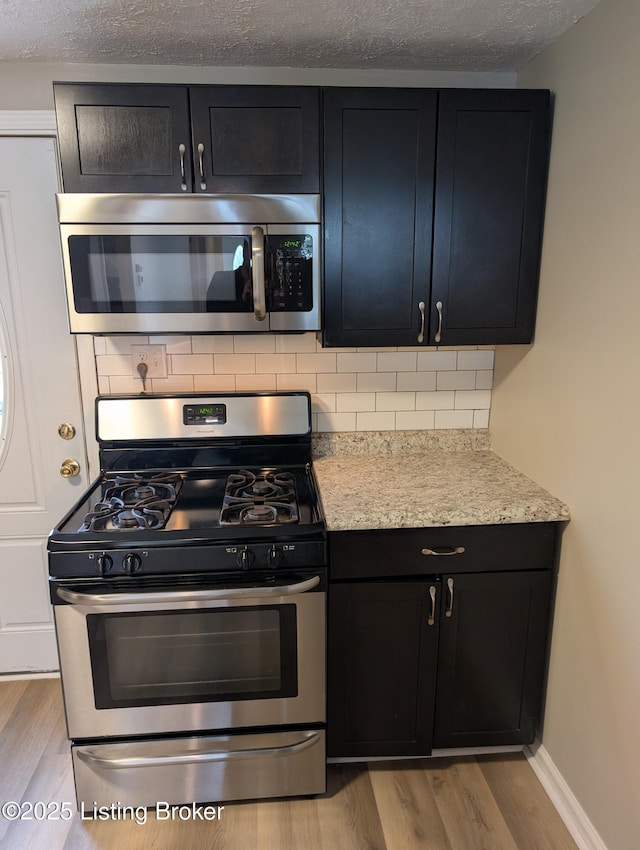 kitchen featuring backsplash, dark cabinetry, light wood-style floors, and stainless steel appliances
