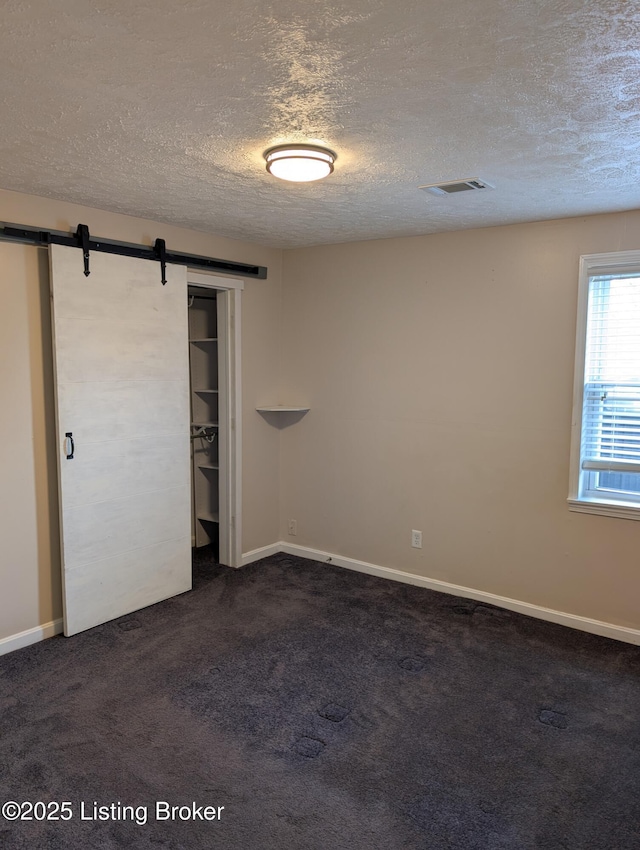 spare room with dark colored carpet, a barn door, visible vents, and a textured ceiling