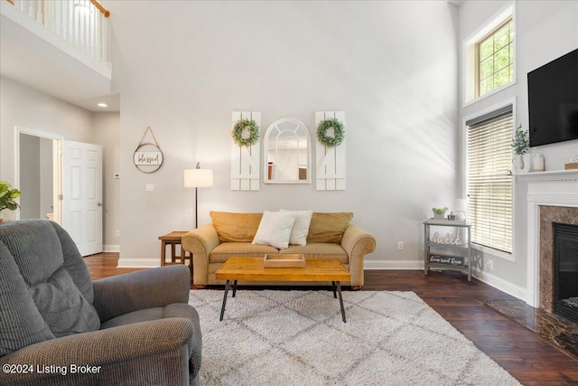 living area featuring a high end fireplace, dark wood-style flooring, a high ceiling, and baseboards