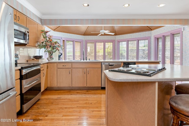 kitchen with a kitchen breakfast bar, wallpapered walls, light countertops, appliances with stainless steel finishes, and a sink