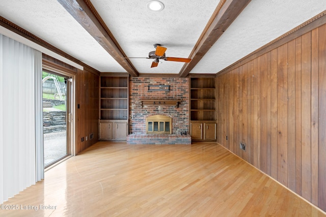 unfurnished living room with a textured ceiling, wood walls, a brick fireplace, beam ceiling, and wood finished floors