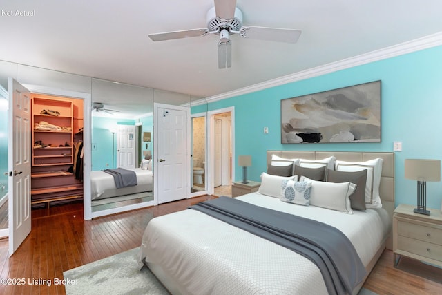 bedroom with a walk in closet, wood-type flooring, a closet, and ornamental molding
