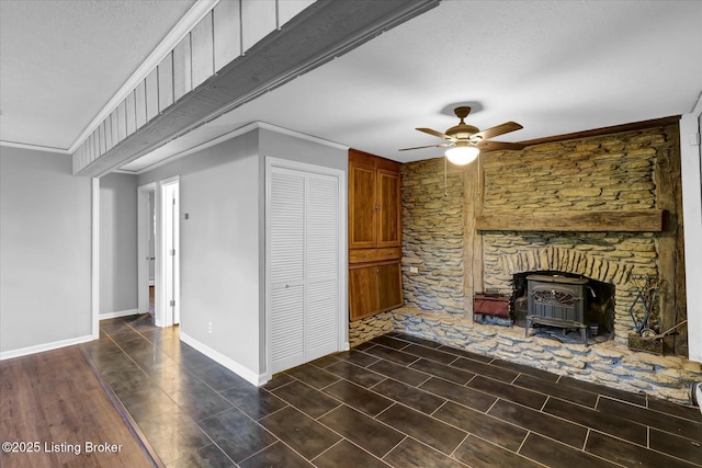 unfurnished living room with baseboards, a textured ceiling, crown molding, a wood stove, and ceiling fan