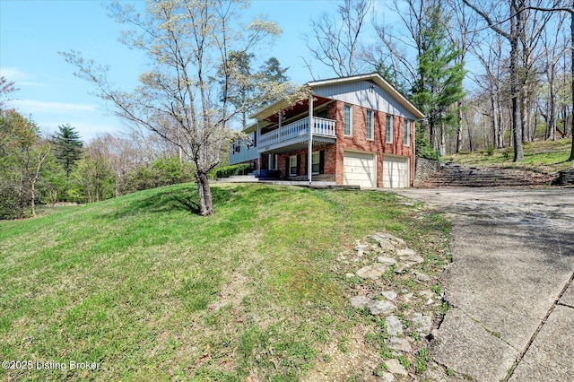 exterior space featuring a garage, brick siding, a front yard, a balcony, and driveway