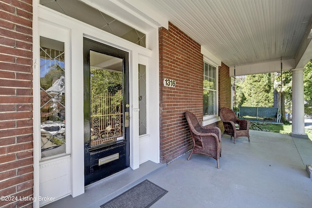 view of exterior entry with a porch and brick siding