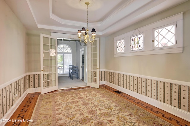 unfurnished dining area featuring french doors, wood finished floors, a tray ceiling, and wallpapered walls