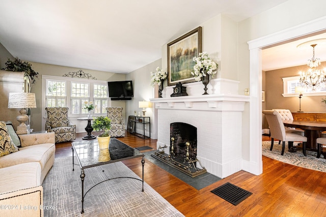 living area featuring visible vents, baseboards, a brick fireplace, a chandelier, and wood finished floors