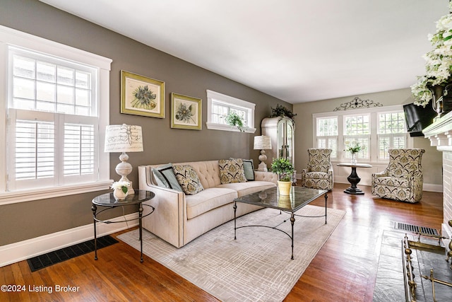living room featuring a fireplace, visible vents, baseboards, and wood finished floors