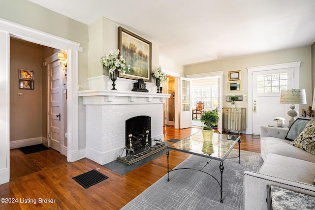 living room with radiator, a fireplace, visible vents, wood finished floors, and baseboards