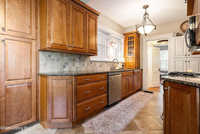 kitchen featuring a sink, appliances with stainless steel finishes, brown cabinetry, dark stone counters, and decorative backsplash