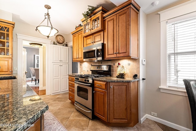 kitchen featuring glass insert cabinets, brown cabinetry, tasteful backsplash, a sink, and stainless steel appliances