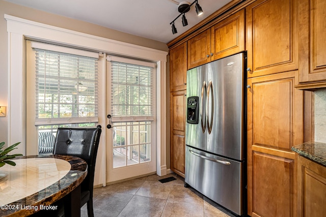 kitchen with brown cabinetry, dark stone counters, stainless steel fridge with ice dispenser, and a wealth of natural light