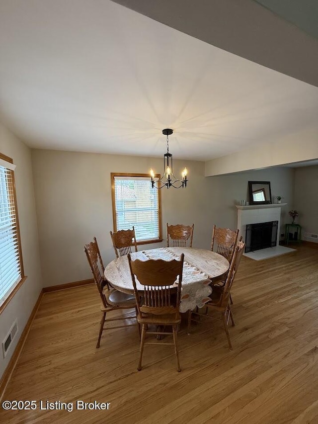 dining space featuring baseboards, an inviting chandelier, a fireplace with flush hearth, light wood-style floors, and visible vents