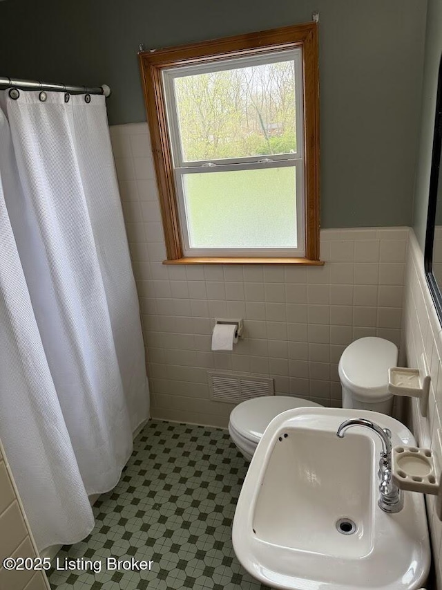 bathroom with toilet, a sink, visible vents, and tile walls