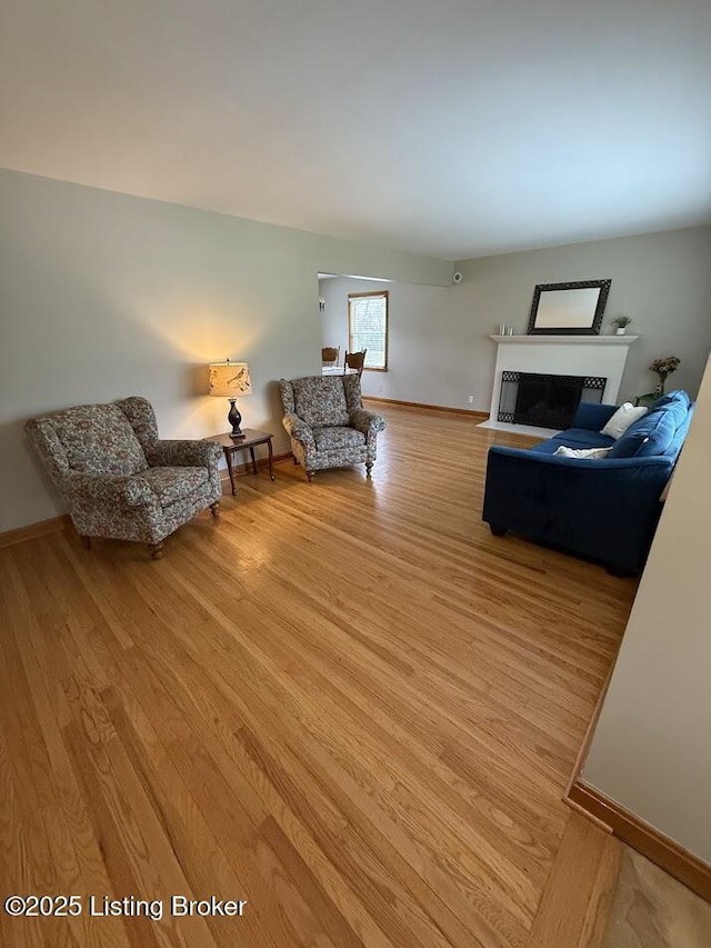 living room featuring a fireplace with flush hearth, light wood-type flooring, and baseboards
