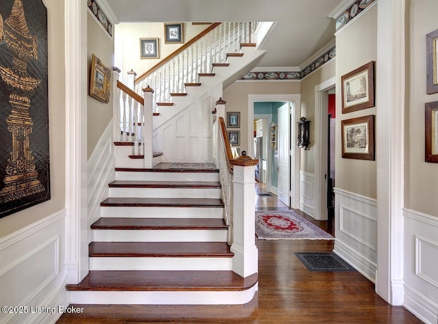 stairway with a decorative wall, wood finished floors, visible vents, and a wainscoted wall