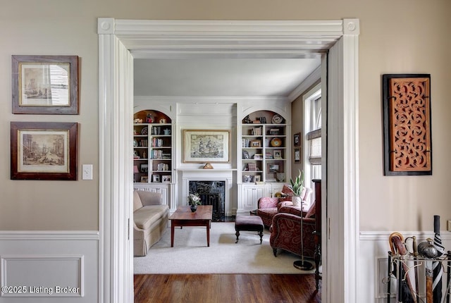 living area with a high end fireplace, built in shelves, dark wood-style flooring, and wainscoting