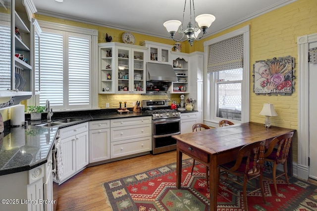 kitchen featuring exhaust hood, open shelves, a sink, a notable chandelier, and range with two ovens