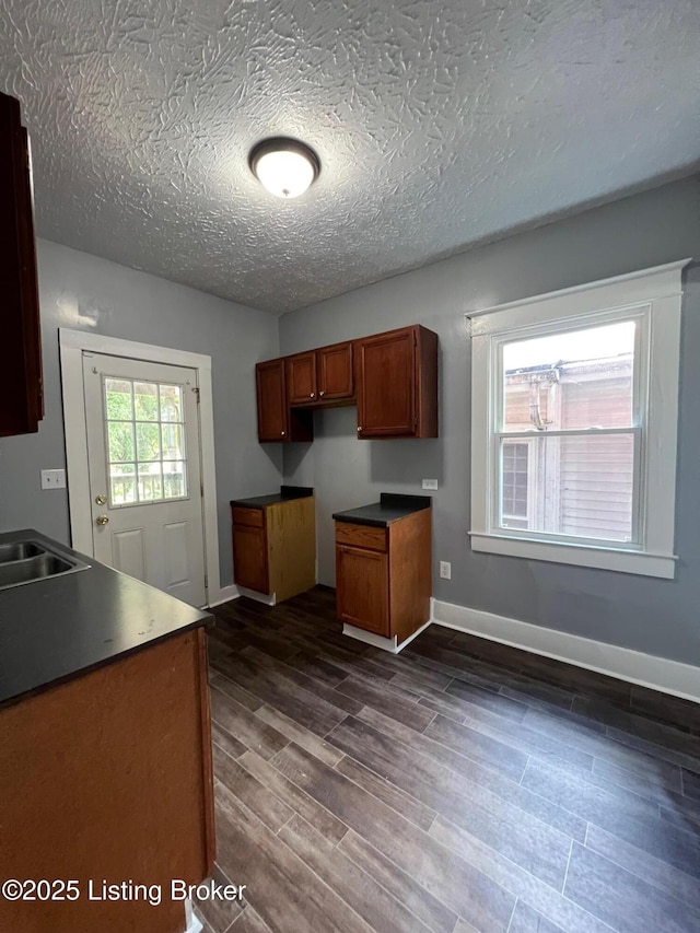 kitchen featuring brown cabinetry, a textured ceiling, a sink, baseboards, and dark wood-style floors