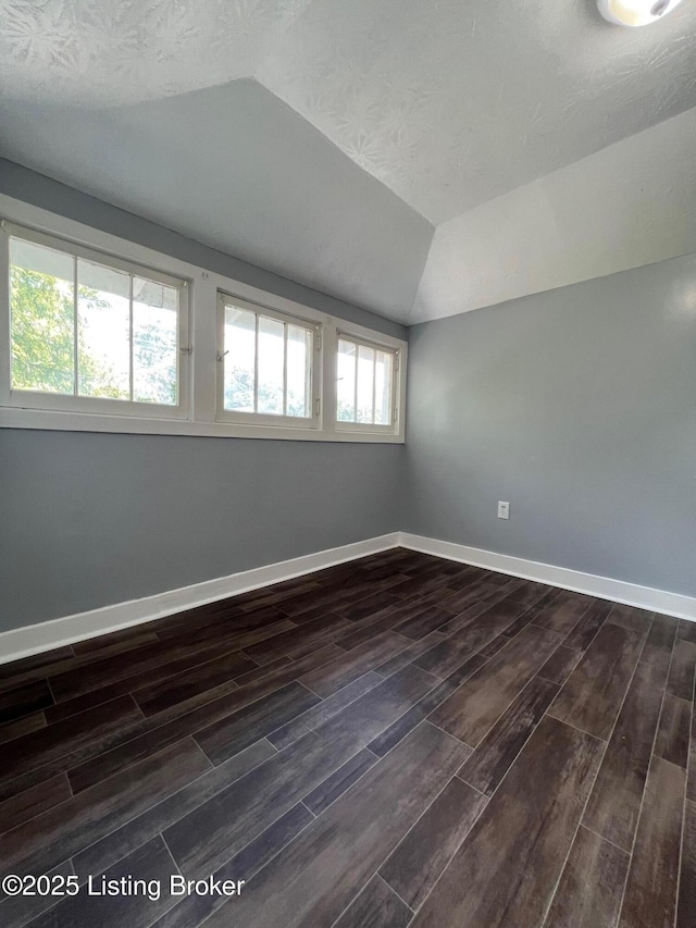 spare room featuring baseboards, vaulted ceiling, and dark wood-style floors