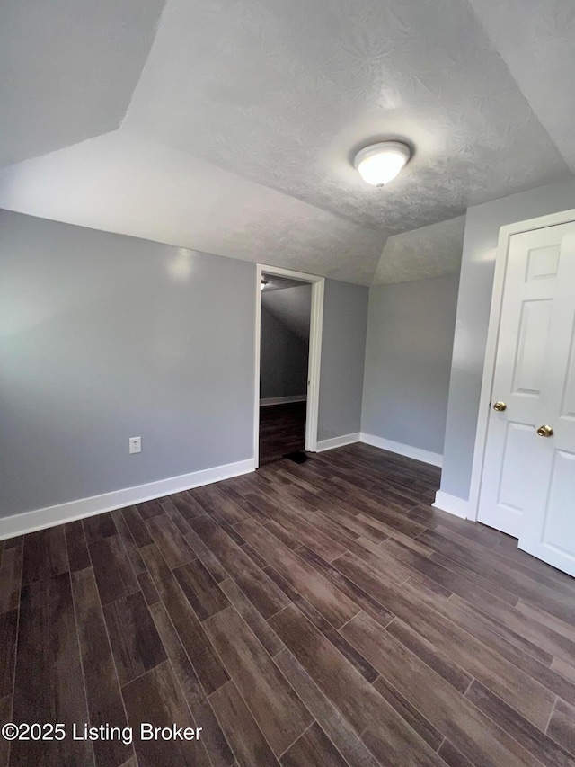 spare room featuring a textured ceiling, dark wood-style flooring, baseboards, and vaulted ceiling