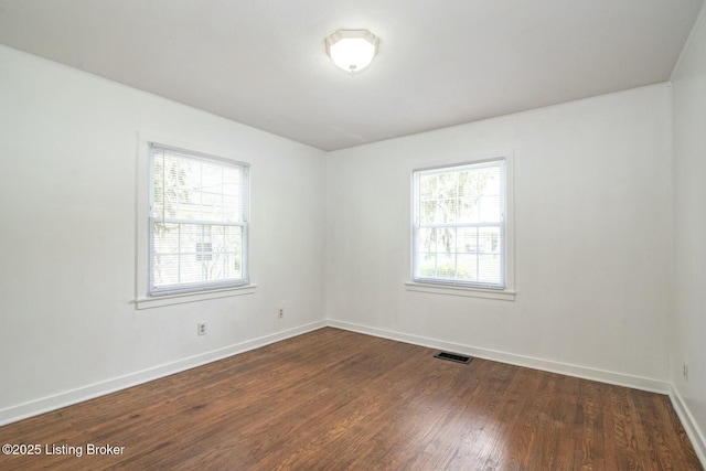 spare room with a healthy amount of sunlight, baseboards, dark wood finished floors, and visible vents